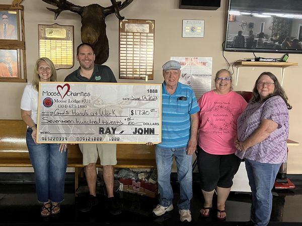 A few people from God's Hands at Work stand in front of a check presentation sign from Moose Lodge members.