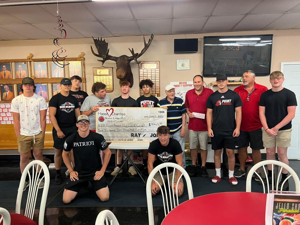 Several football players stand in front of a check presentation sign from Moose Lodge members.