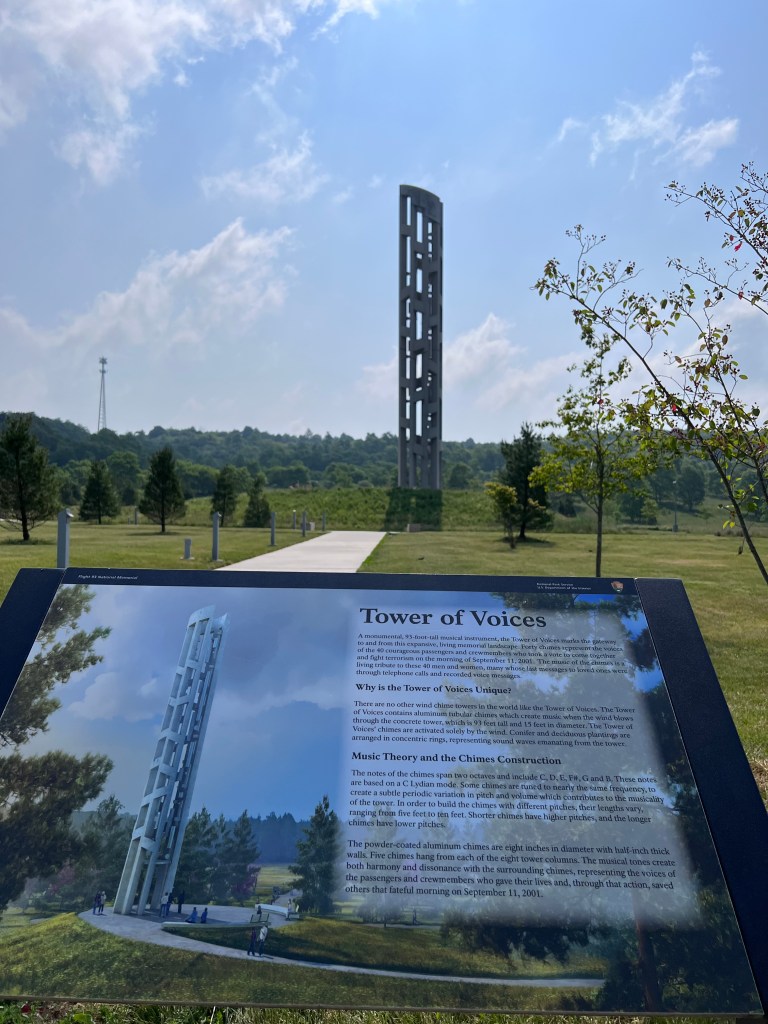 A large concrete memorial in the distance with a sign in the foreground explaining the Tower of Voices.