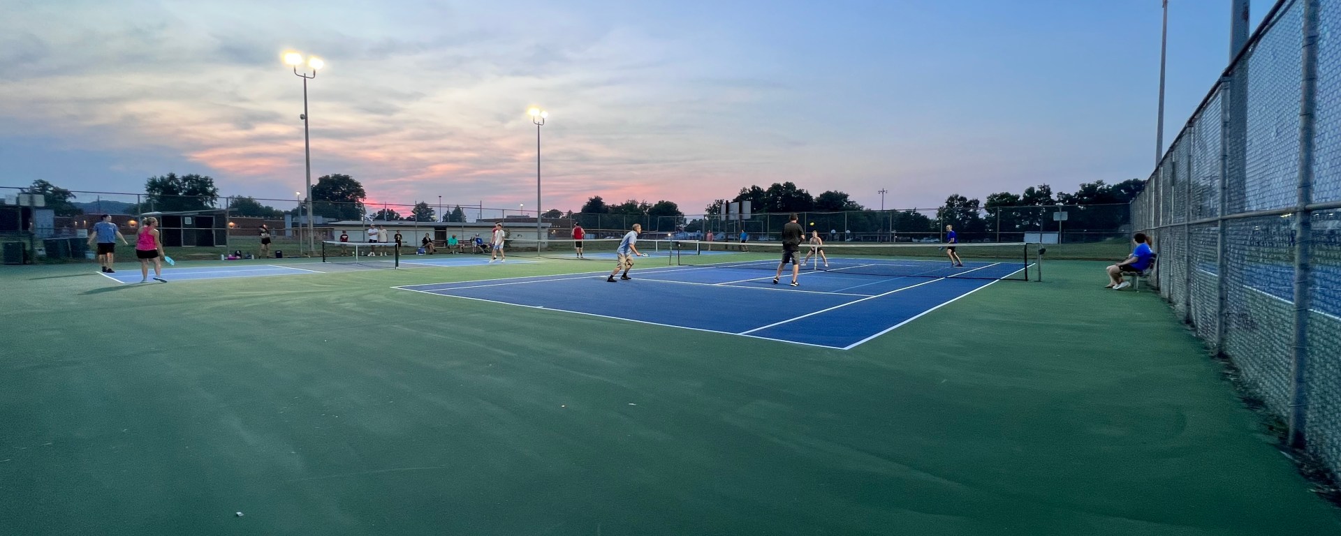 People fill up three pickleball courts at sunset, playing games.