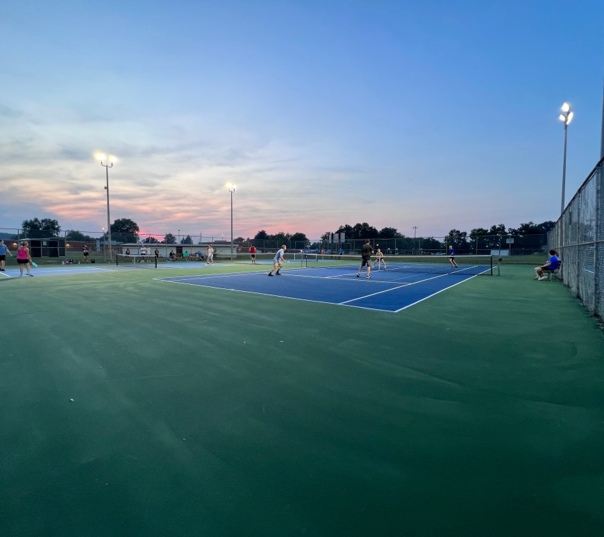 People fill up three pickleball courts at sunset, playing games.