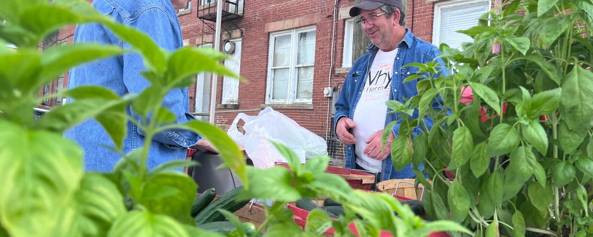 A man speaks to a woman purchasing produce at an open air market.