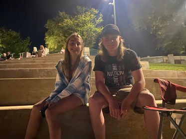 Two teens sit in the amphitheater during a nighttime concert. 