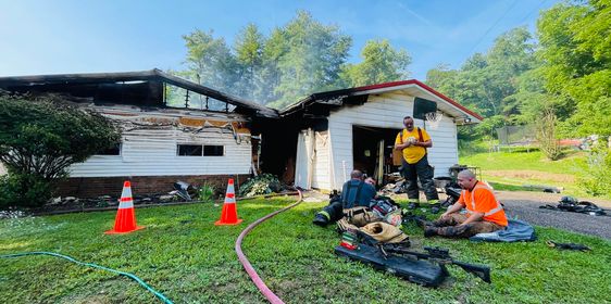 Firefighters sit on the ground to rest following extinguishing a fire at a home with heavy damage. 