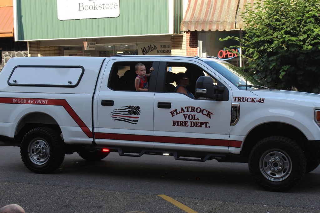 A young man sticks his head out of the back window of a fire station's pickup.