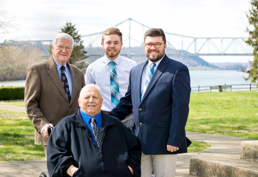 Four members of a quartet are pictured at a park, a bridge and river is behind them.