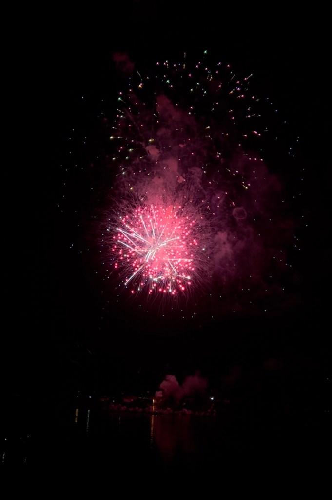 Red and pink fireworks in a dark night sky, over the Ohio River.