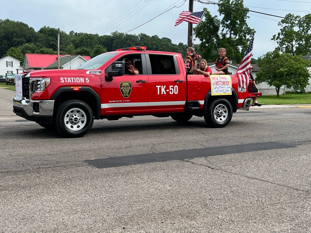 A truck from the fire department transports members of a softball team in the truck bed. 