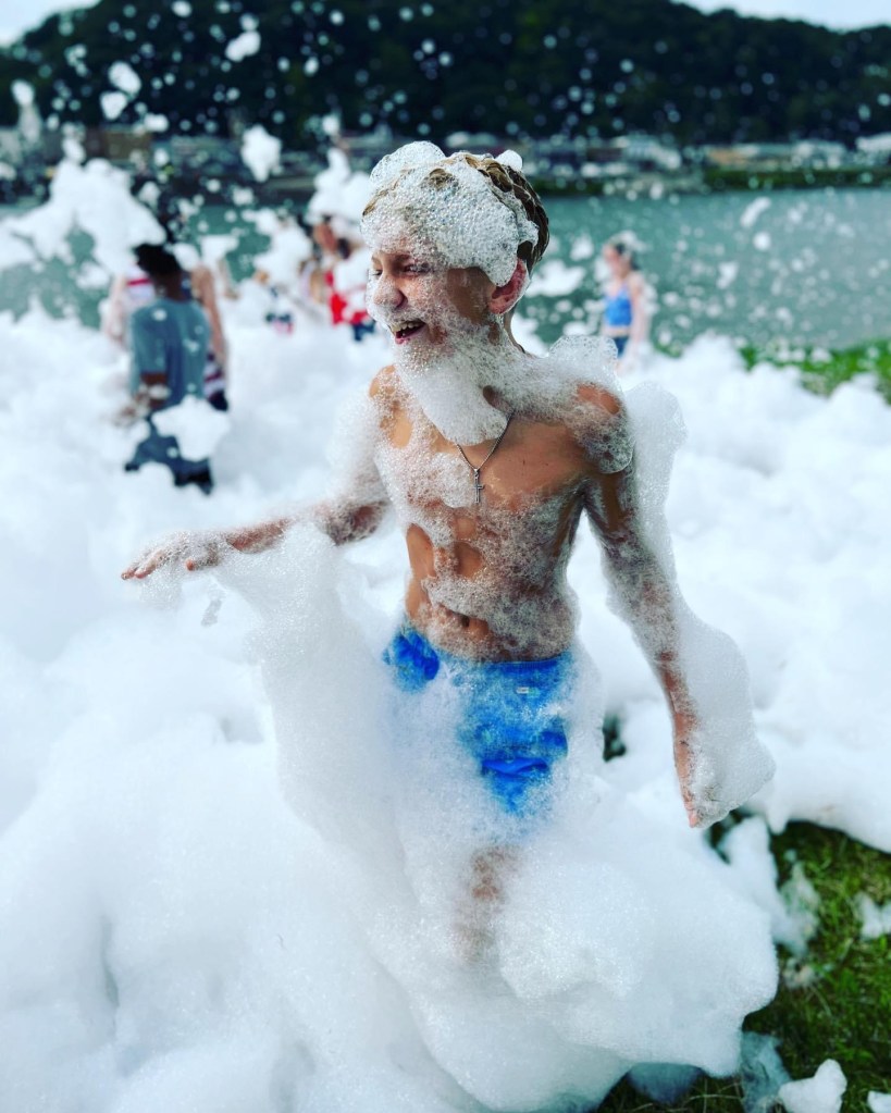 A young boy smiles while covered in foam.