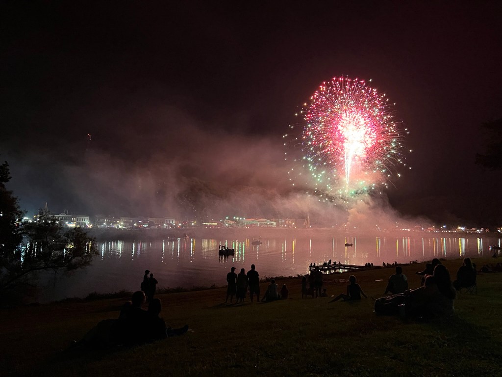 Fireworks explode over the Ohio River with boaters and people gathered along the banks pictured. 