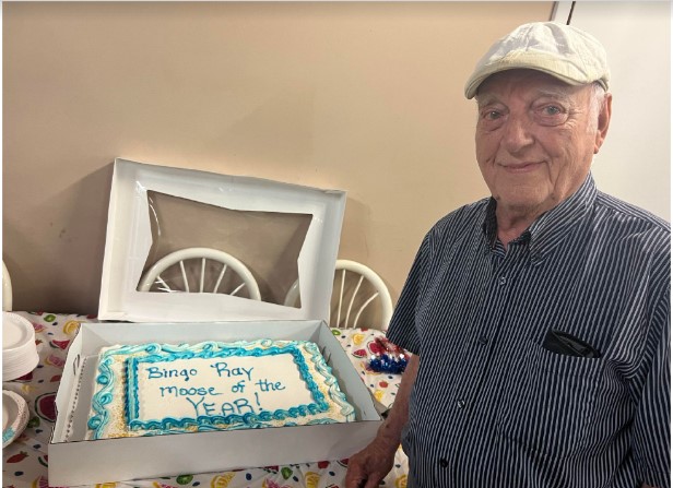 A man stands near a cake celebrating his award. 