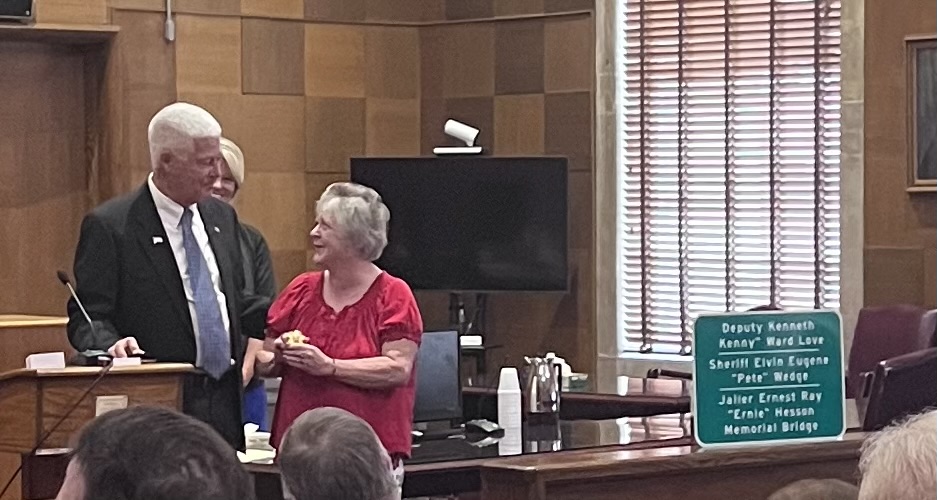 Three people are at a podium as one woman is presented a small box containing her father's badge. 