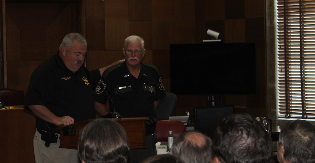 Two men stand at a podium as one speaks to those seated.