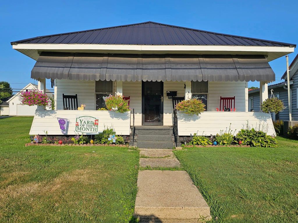 Pictured with a "Yard of the Month" sign, is a decorated yard, with flowers and landscaping surrounding a home. 