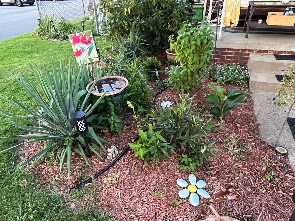 Pictured with a "Yard of the Month" sign, is a decorated yard, with flowers and landscaping surrounding a home. 