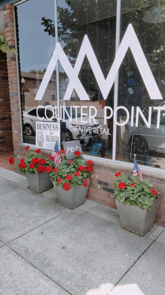 Pictured with a "Business in Bloom" sign, is a decorated storefront, with flowers and landscaping surrounding a business. 