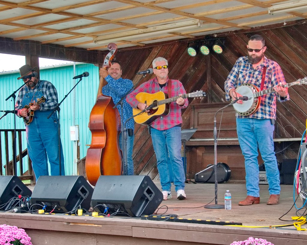 A four-piece band plays. Instruments include mandolin, upright bass, guitar, banjo.