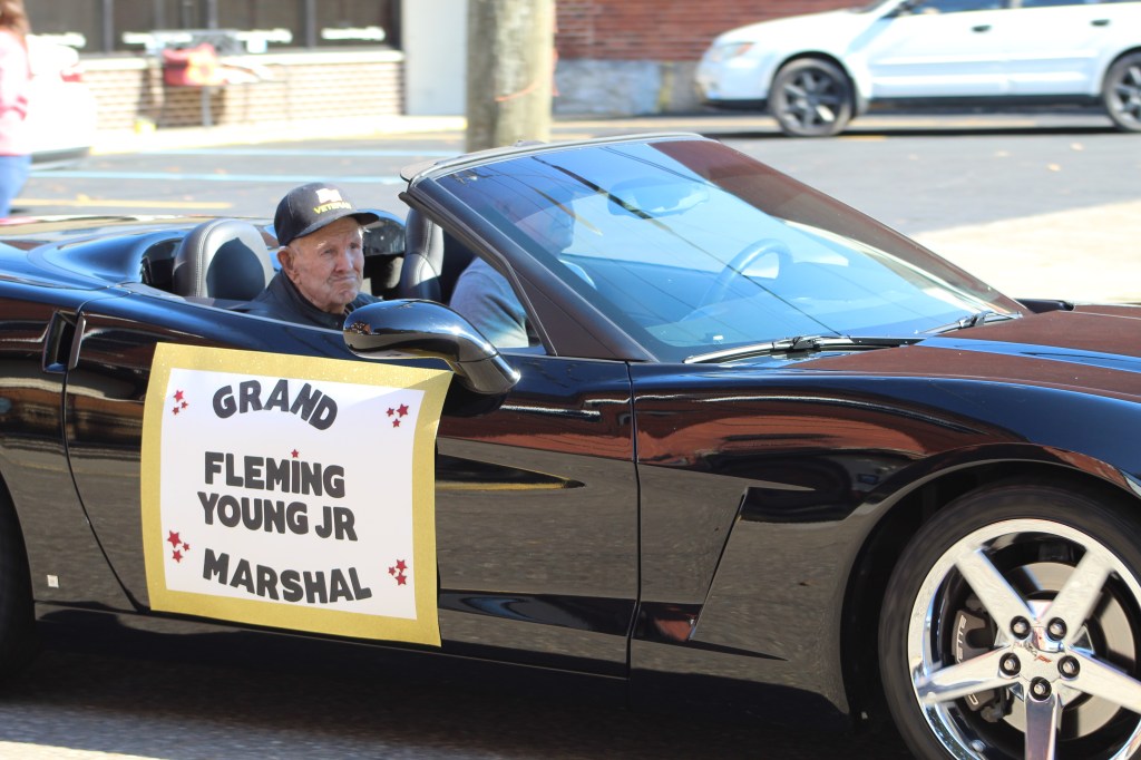 The grand marshal rides in a black convertible.  