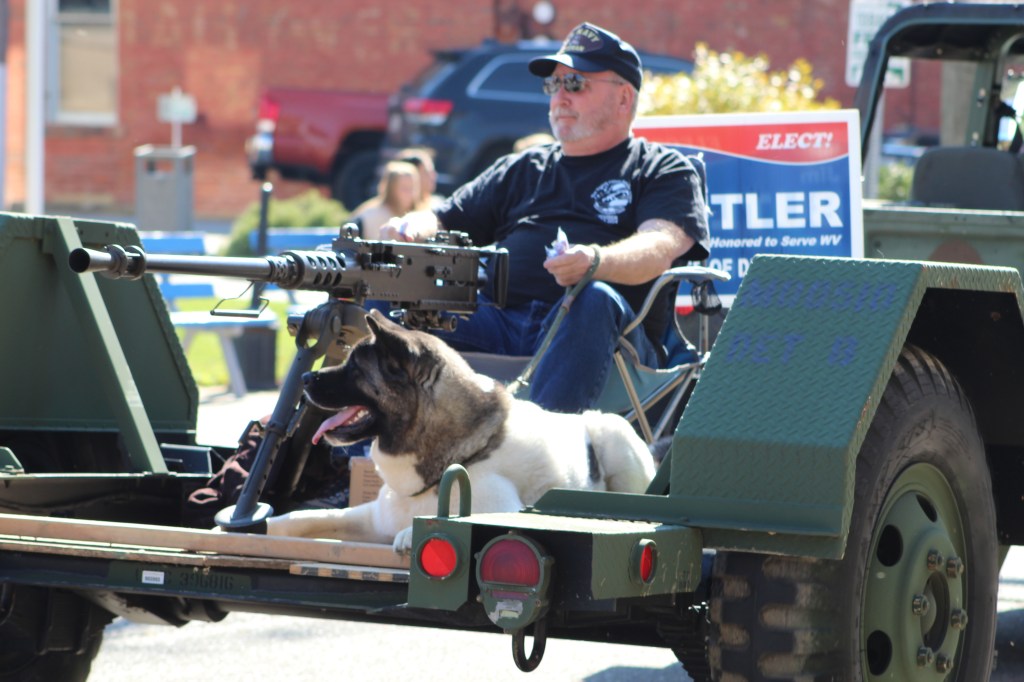 A man rides a float with a large dog and gun on display.
